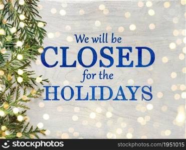 Signboard with the inscription We will be closed for the holidays and green branches of a Christmas tree. View from above, closeup, indoors, no people. Congratulations for family, friends, colleagues. We&rsquo;ll be closed for the holidays. Signboard