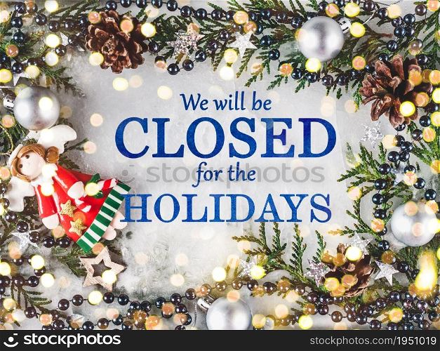 Signboard with the inscription We will be closed for the holidays and green branches of a Christmas tree. View from above, closeup, indoors, no people. Congratulations for family, friends, colleagues. We&rsquo;ll be closed for the holidays. Signboard