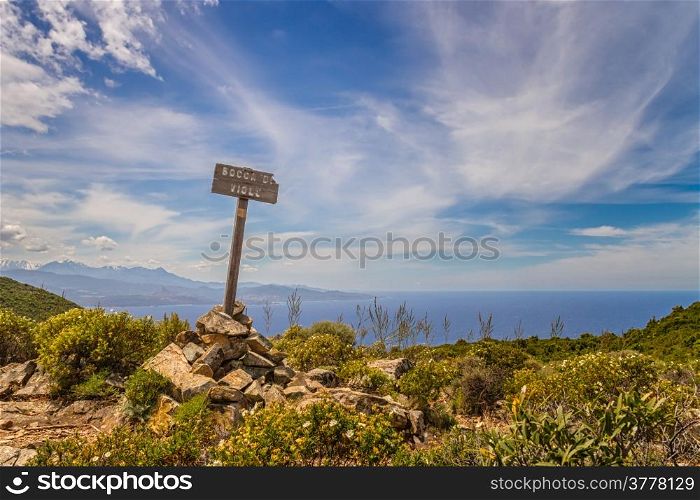 Signpost marking the top of Bocca di Violu near Nonza on Cap Corse in Corsica with snow capped mountains and Desert des Agriates in the background