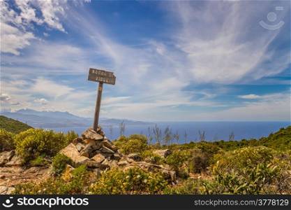 Signpost marking the top of Bocca di Violu near Nonza on Cap Corse in Corsica with snow capped mountains and Desert des Agriates in the background
