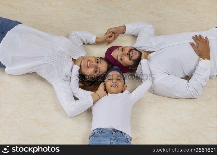 SIKH BOY HAPPILY HUGGING MOTHER AND FATHER WHILE LYING ON FLOOR AND POSING