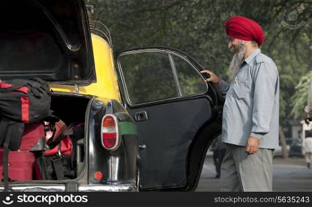 Sikh taxi driver holding the door of the vehicle open
