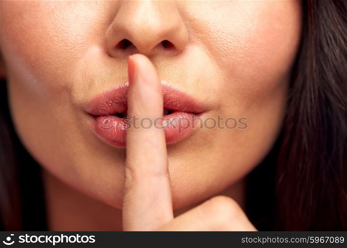 silence, gesture and beauty concept - close up of young woman holding finger on lips