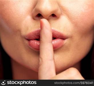 silence, gesture and beauty concept - close up of young woman holding finger on lips