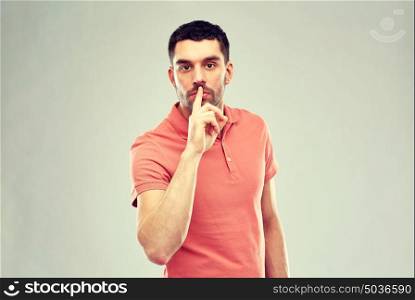 silence, gesture and people concept - serious young man making hush sign over gray background. young man making hush sign over gray background