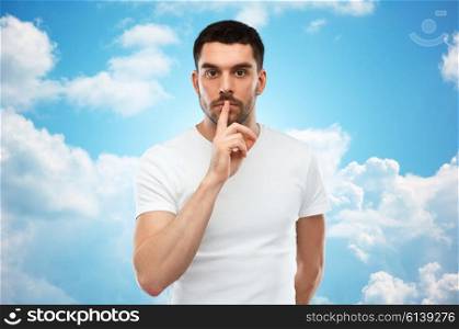 silence, gesture and people concept - young man making hush sign over blue sky and clouds background