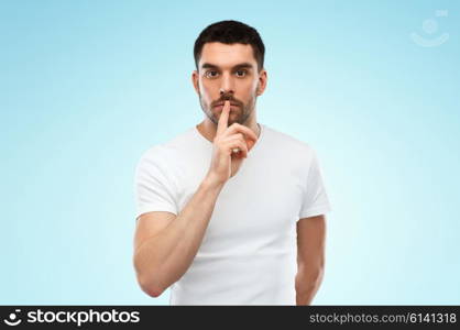 silence, gesture and people concept - young man making hush sign over blue background