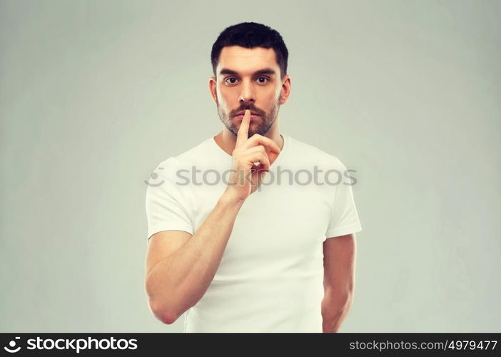 silence, gesture and people concept - young man making hush sign over gray background. young man making hush sign over gray background