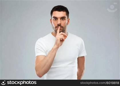 silence, gesture and people concept - young man making hush sign over gray background