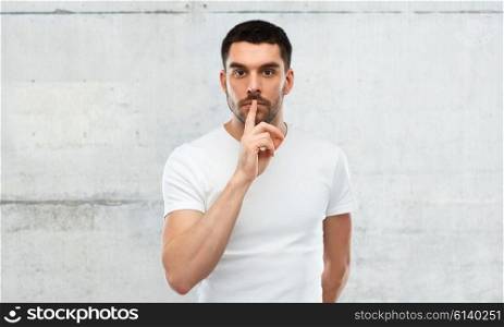 silence, gesture and people concept - young man making hush sign over gray wall background