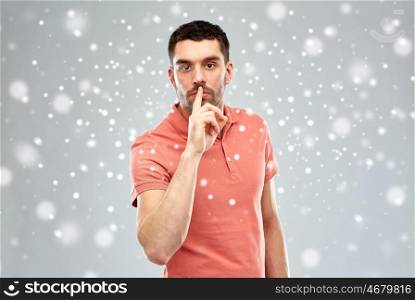 silence, gesture, winter, christmas and people concept - serious young man making hush sign over snow on gray background