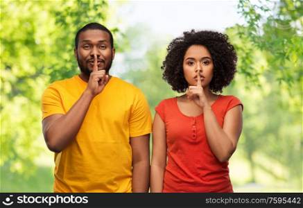 silence, secret and confidentiality concept - happy african american couple making hush gesture over green natural background. happy african american couple making hush gesture
