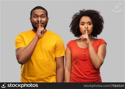 silence, secret and confidentiality concept - happy african american couple making hush gesture over grey background. happy african american couple making hush gesture