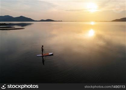 Silhouette Aerial view of stand up paddle boarder paddling at sunset on a flat warm quiet river.