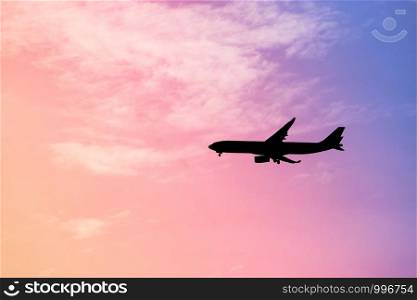 Silhouette an airplane in flight against rainbow colorful sky and clouds. Abstract pastel beautiful landscape at sunset.