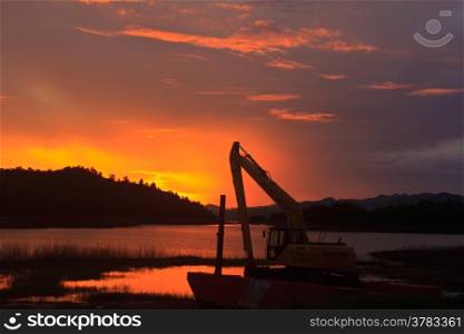 Silhouette Backhoe, machine in worksite near lake on sunset