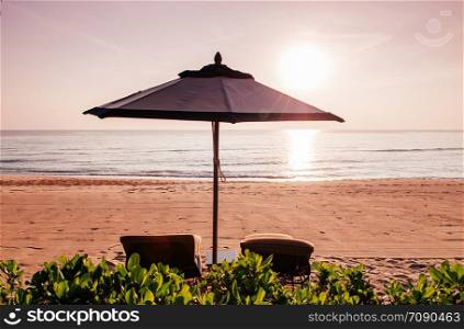 silhouette Beach bed under umbrella behind green bush on tropical beach against sunset - Thailand summer island concept