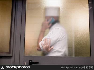 silhouette behind the glass of a man in a chef"s uniform talking on the phone