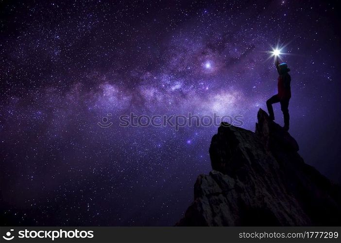Silhouette climber or backpacker, he held the light up high above his head. Standing on rocky mountain peak against Milky way galaxy, stars and space dust in the universe, success, leader concept.. Leader on top.