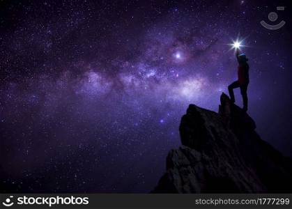Silhouette climber or backpacker, he held the light up high above his head. Standing on rocky mountain peak against Milky way galaxy, stars and space dust in the universe, success, leader concept.. Leader on top.