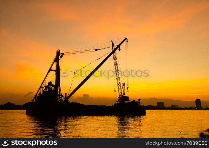Silhouette construction site floating over river with reflection on sunset. Construction concept.