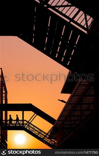 Silhouette couple office workers walking on footbridge connecting the buildings against sunset sky background in evening time, low angle view and vertical frame
