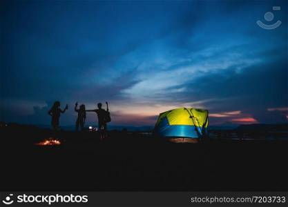 Silhouette group of Asian friends tourist drinking and playing guitar together with happiness in Summer while having camping near lake