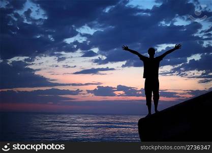 Silhouette guy placed hands in sides on breakwater in evening near sea