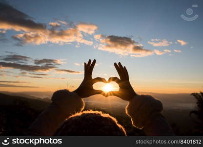 Silhouette hands forming a heart shape with sunrise