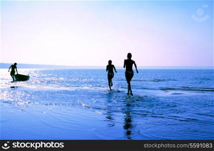 silhouette image of two running girls and muscular man in water