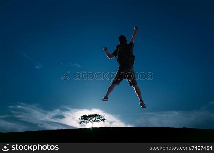 Silhouette image of young guy cheer and jump up with cold tone sunset landscape . success, leadership and achievement concept .