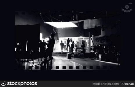 Silhouette images of video production behind the scenes or b-roll or making of TV commercial movies that film crew team lightman and videos cameraman working together with movie director in studio.