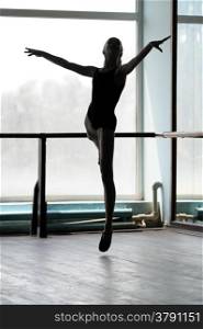 Silhouette of a ballerina making arabesque in the air. Shot against the window with sunlight