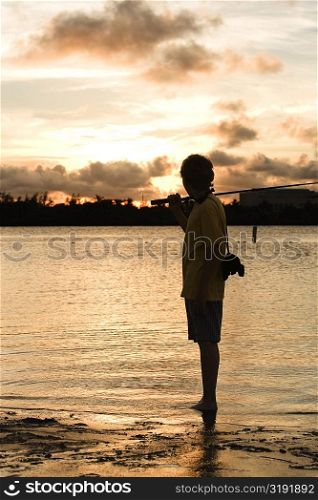Silhouette of a boy carrying a fishing rod