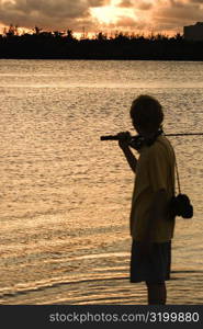 Silhouette of a boy carrying a fishing rod