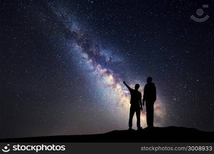 Silhouette of a father and a son who pointing finger in night starry sky on the background of Milky Way. Family. Colorful night landscape. Beautiful Universe. Space. Travel background with sky full of stars