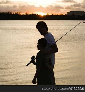Silhouette of a father and his son carrying a fishing rod