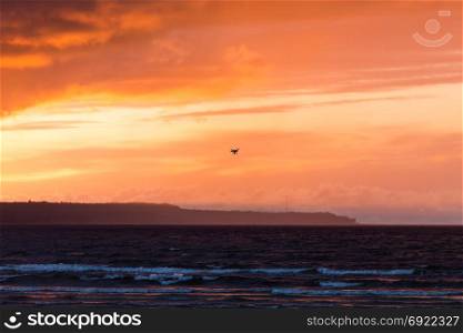 Silhouette of a flying drone in clouds sky on a background of sea sunset