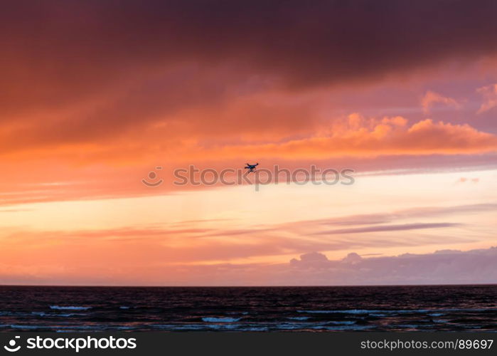 Silhouette of a flying drone in clouds sky on a background of sea sunset