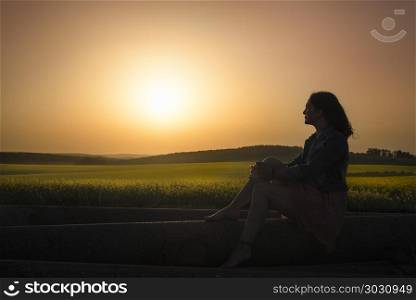 Silhouette of a girl and sunset over canola fields. Silhouette of a woman gazing the horizon, admiring the sunset over rapeseed fields, in South Moravia, Czech Republic.
