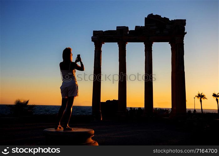 Silhouette of a girl photographing on the phone the Temple of Apollo at sunset. Side, Turkey. Silhouette of girl photographing on phone Temple of Apollo at sunset