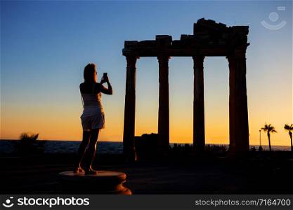 Silhouette of a girl photographing on the phone the Temple of Apollo at sunset. Side, Turkey. Silhouette of girl photographing on phone Temple of Apollo at sunset