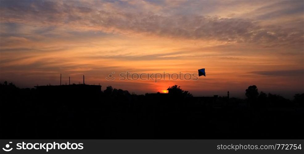 Silhouette of a kite flying in the open sky over a city in summer season, with a beautiful sunset in the background