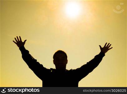 Silhouette of a man against the background of the sun and yellow at sunset sky. Hands are raised up to the sun. Silhouette of a man against the background of the sun and yellow at sunset sky. Hands are raised up to the sun.