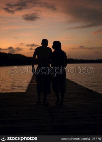 Silhouette of a man and a woman walking on a pier