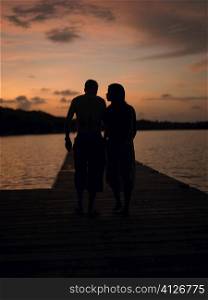 Silhouette of a man and a woman walking on a pier