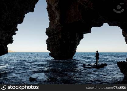 Silhouette of a man diving into water, view from a cave