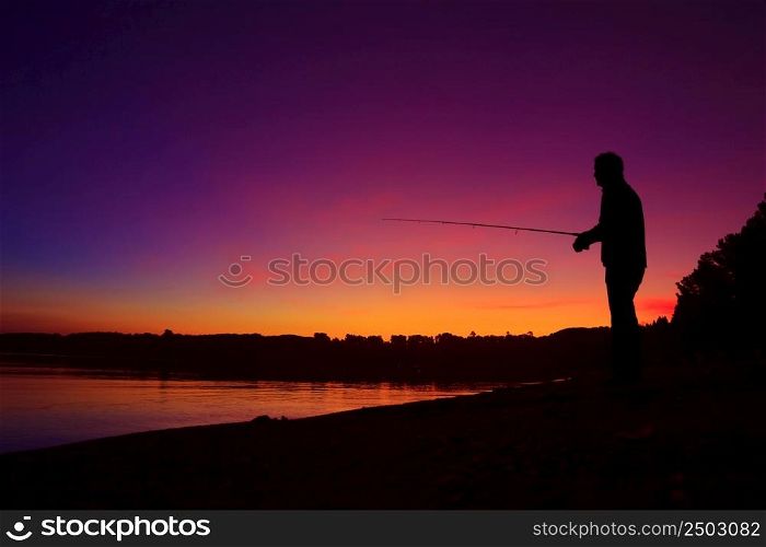 Silhouette of a man fishing on the lake shore at sunset