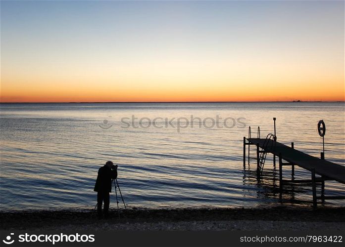Silhouette of a man photographing the sunset by a bath pier