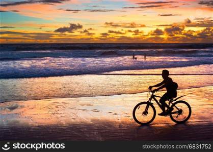 Silhouette of a man riding a bicycle at sunset on the beach. Bali island, Indonesia